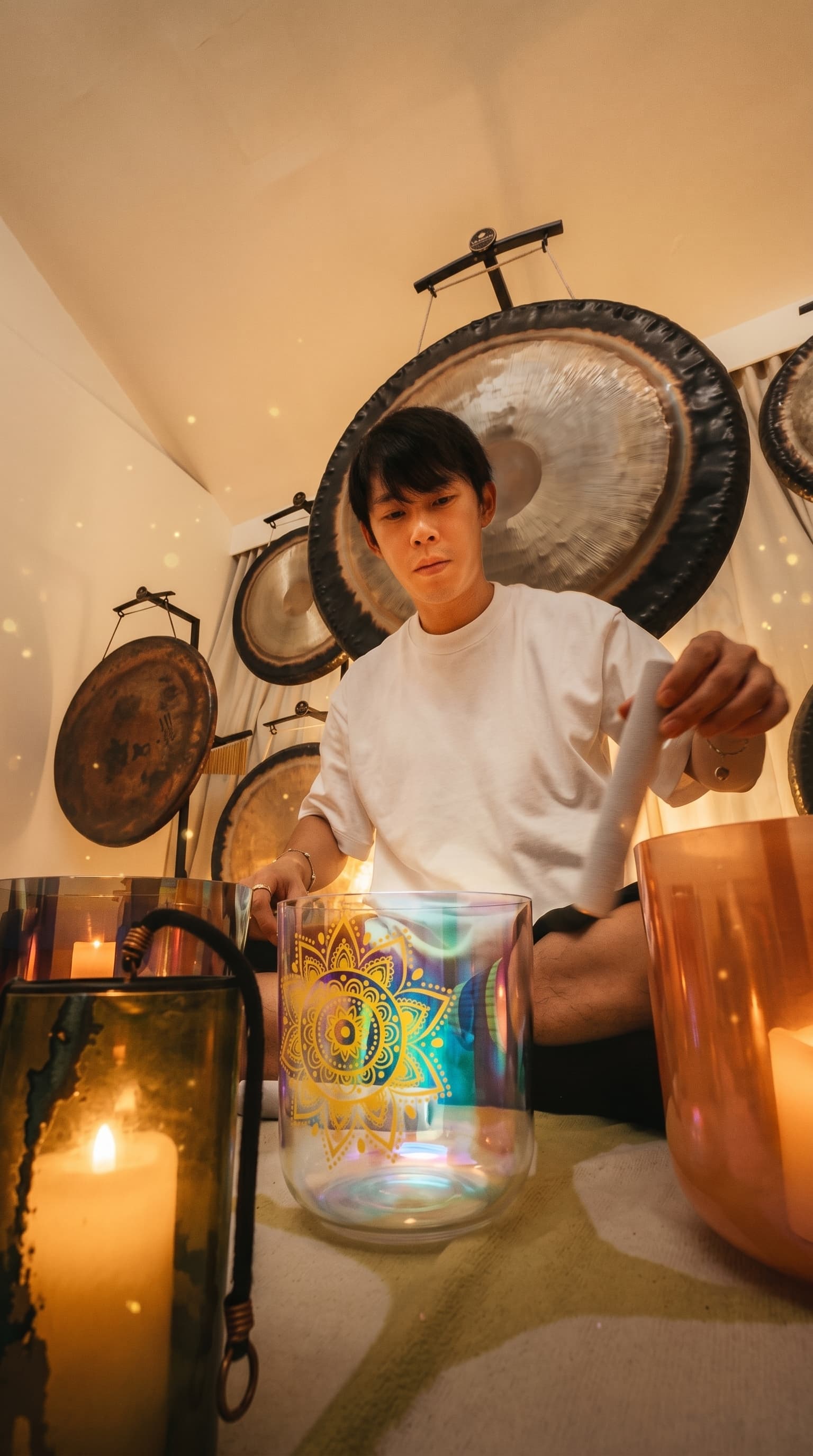 Teepee playing a crystal singing bowl in a candlelit studio, surrounded by gongs